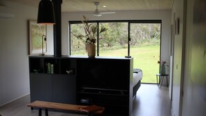 Una sala de estar moderna con chimenea empotrada, un banco, un televisor y un amplio ventanal con vistas al exterior.