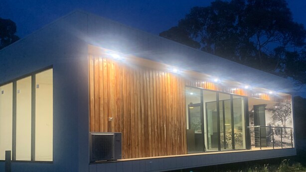 Un edificio moderno con amplios ventanales, paneles de madera y una puerta de vidrio que da a un espacio exterior.