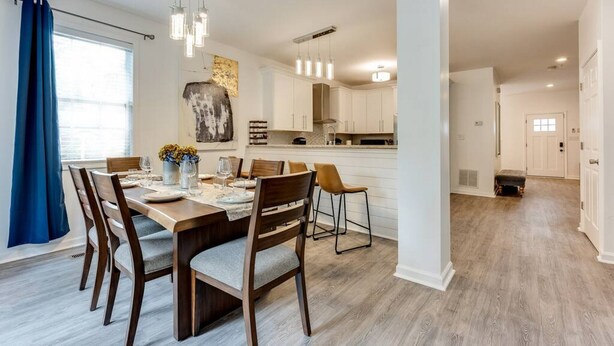 Una cocina moderna con armarios blancos, una mesa de comedor de madera e iluminación colgante.