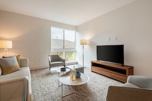 Ein modernes Wohnzimmer mit Sofa, Sessel, Couchtisch, Fernseher und Stehlampe.