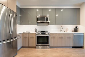 A modern kitchen with stainless steel appliances, wooden cabinets, and a tiled backsplash.