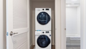 A laundry room with two stacked front-loading washing machines and a bathtub. - Luxury One Bedroom with Full-Service Amenities (Mountain View)