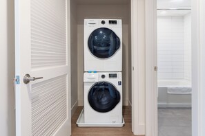 Ein Waschraum mit zwei übereinander gestapelten Waschmaschinen und einer Badewanne.