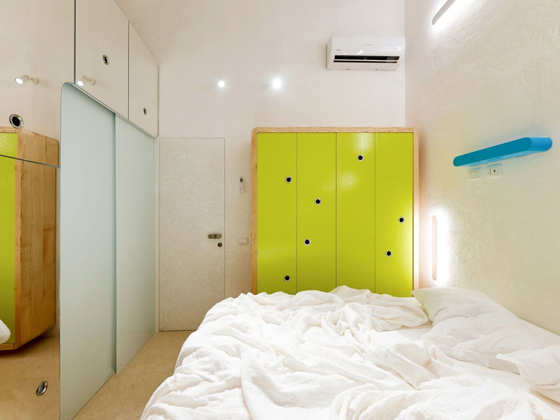 Een slaapkamer met een bed, een groene garderobe, een witte airconditioner en een blauwe lichtschakelaar aan de muur.