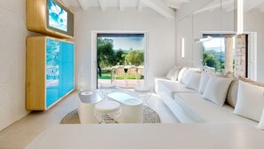 Ein modernes Wohnzimmer mit einem weißen Sofa, einem Couchtisch und einem blauen Schrank. Ein großes Fenster bietet einen Blick ins Freie.