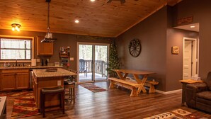 Amplia sala de estar con techo de madera, cocina con encimeras de granito, mesa de comedor y un árbol de Navidad.
