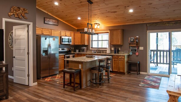 Una cocina amplia con armarios de madera, una isla central con taburetes de bar, un refrigerador y un microondas.