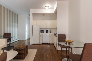 Cocina moderna con armarios blancos, lavavajillas y microondas. Hay una zona de comedor con mesa de vidrio y sillas marrones.