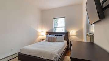 A bedroom with a bed, bedside lamps, a window, and a flat-screen TV mounted on the wall.