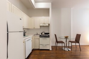 Una cocina compacta con muebles blancos, una estufa y una zona de comedor con dos sillas y una mesa pequeña.