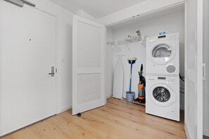 A laundry room with a front-loading washing machine, a mopping bucket, and a vacuum cleaner. - Large Two Bedroom, One Block From Fenway Park (Boston)