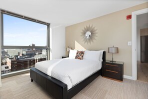 Quarto moderno com uma cama grande, mesa de cabeceira, abajur e vista da cidade através de uma janela ampla.