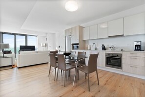 A modern kitchen with white cabinets, a dining area with a glass table, and a large window offering a view. - Large Two Bedroom, One Block From Fenway Park (Boston)