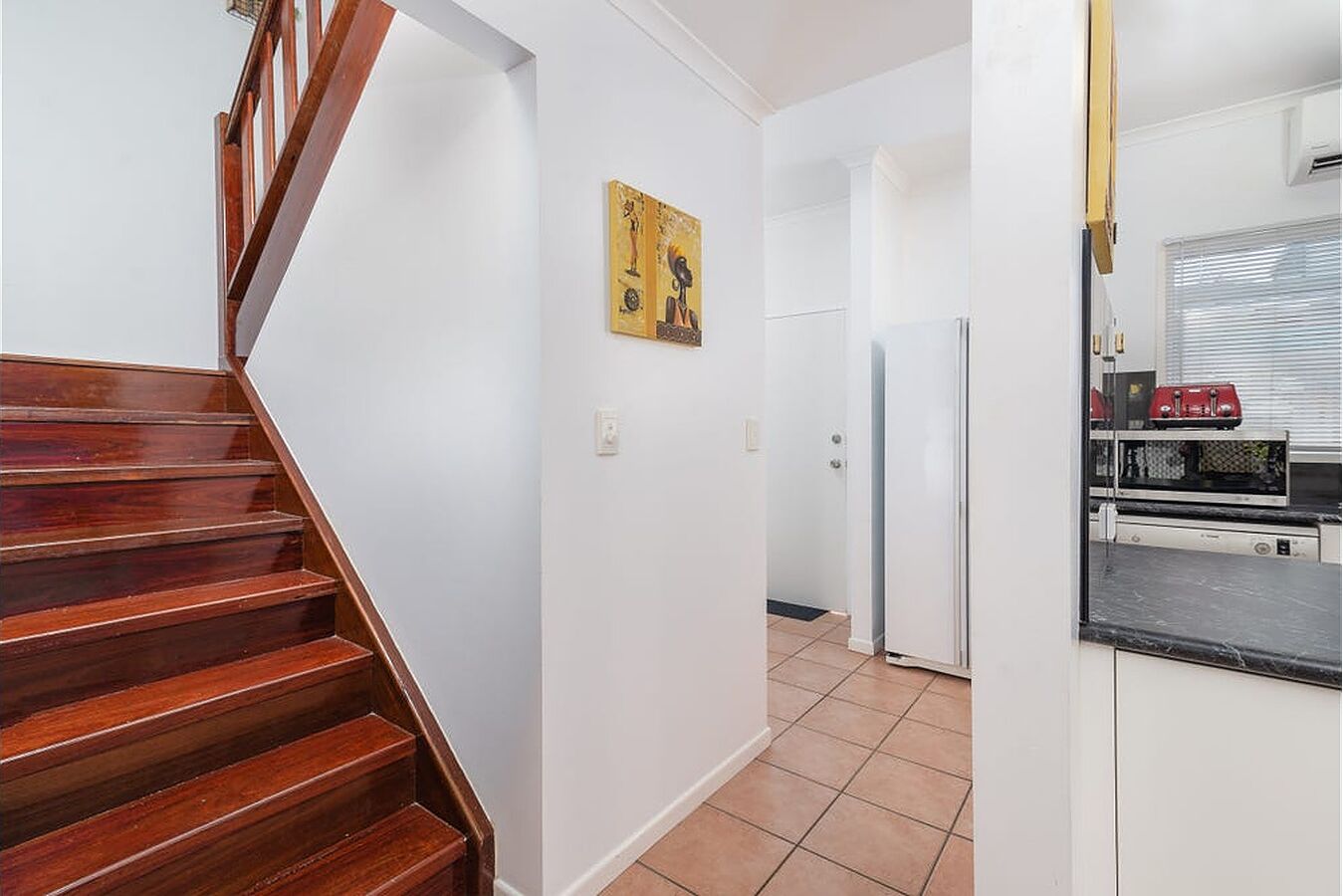 A staircase leading to a kitchen with a refrigerator and a microwave.