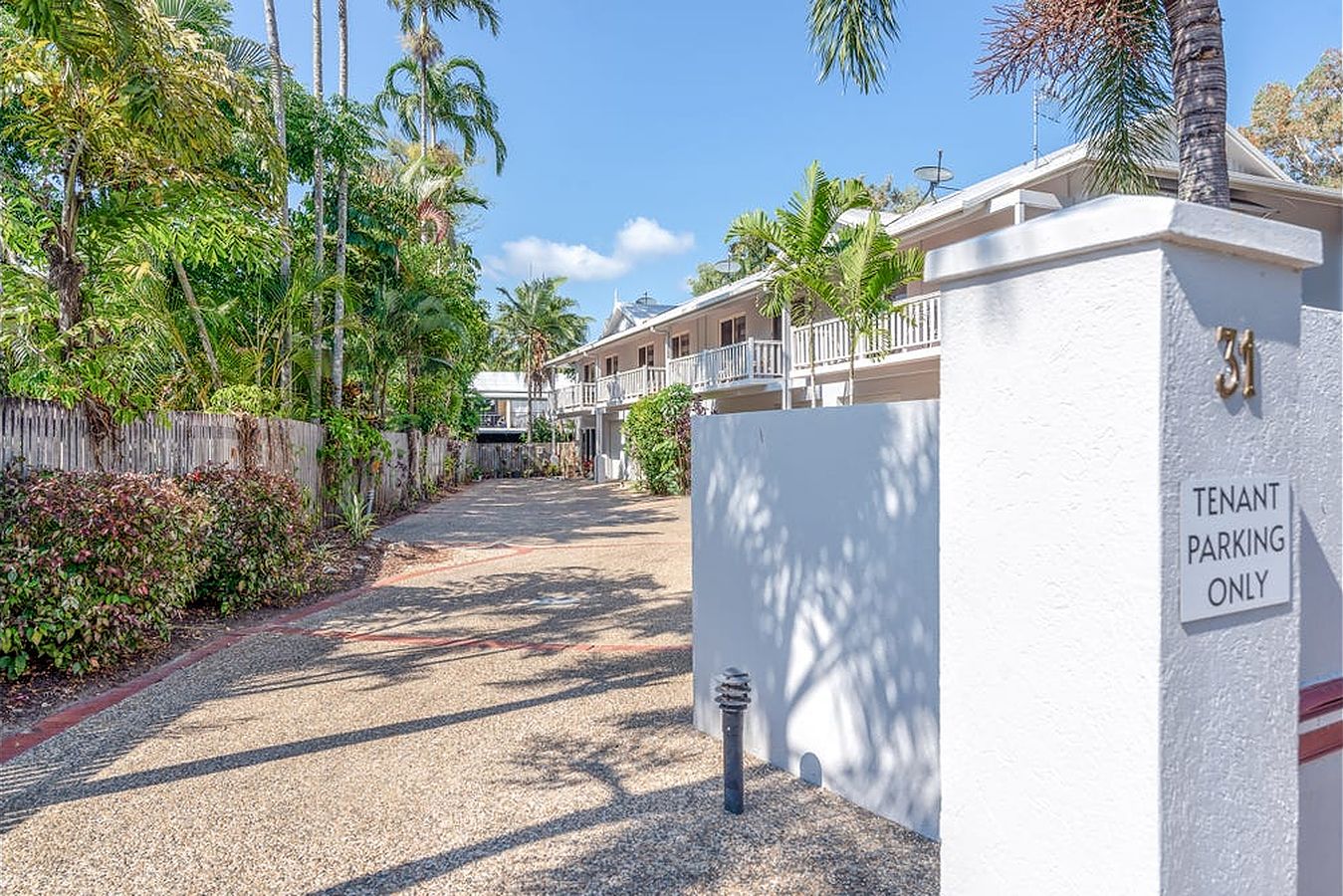 A gated driveway with a 'Tenant Parking Only' sign, surrounded by lush greenery and a clear blue sky.
