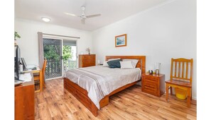 Ein Schlafzimmer mit einem hölzernen Bett, einem Schreibtisch, einem Stuhl, einem Nachttisch und einem Fenster mit Vorhängen.