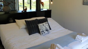 Ein ordentlich bezogenes Bett mit weißer und grauer Bettwäsche, einem blau-weißen Kopfkissen und einem Handtuch daneben.