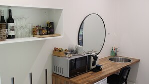 Eine kompakte Küche mit Mikrowelle, Spüle und kleinem Kühlschrank. Es gibt eine Holz Arbeitsplatte, einen Spiegel und ein Regal mit Weinflaschen und Gläsern.