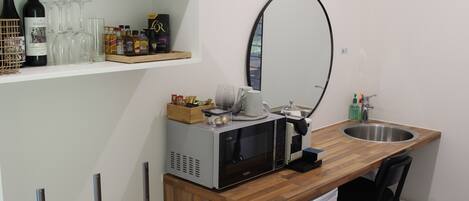 A kitchenette with a microwave, sink, and wine bottles on a shelf.