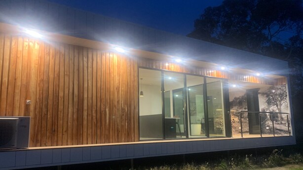 Ein modernes Gebäude mit Holzverkleidung, großen Glasüren und einer sichtbaren Klimaanlage.