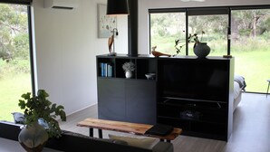 Ein modernes Wohnzimmer mit Kamin, Flachbildfernseher und einem großen Fenster mit Blick ins Freie.