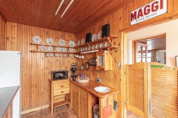 A wooden interior with a kitchen area, including a refrigerator, microwave, and sink. There are wooden cabinets and a sign that reads "MAGGI".