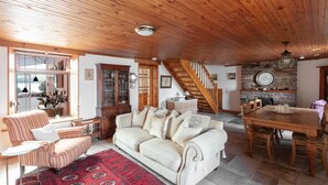 A spacious living area with a wooden ceiling, a sofa, a dining table, and a staircase.