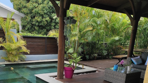 A pool area with a wooden deck, potted plants, and a covered seating area.