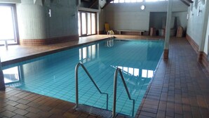 Une piscine intérieure avec un sol carrelé et un escalier pour y accéder.