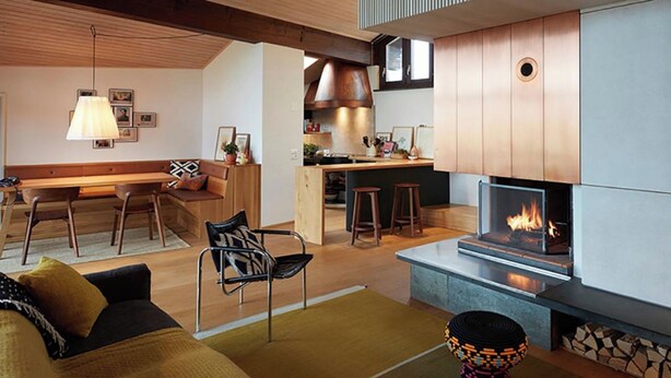 Un intérieur moderne comprenant un canapé, des fauteuils, une table à manger, un coin cuisine avec une cuisinière et une cheminée.