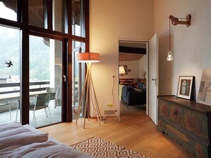A spacious bedroom with a large window, a floor lamp, a patterned rug, and a wooden dresser with a picture frame. - Am Dürrbach 2/244 Appartement/Fewo 6-Bettwohnung by Interhome (Engelberg)