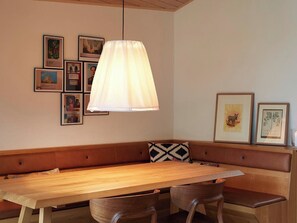 Une table à manger en bois, accompagnée d’un banc, d’un luminaire suspendu et de tableaux encadrés accrochés au mur.