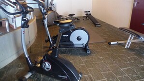 Une salle de sport équipée de divers appareils, notamment un vélo elliptique, un vélo d’appartement et un banc de musculation.