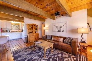 A cozy living room with a wooden ceiling, a brown leather sofa, a coffee table, and a rug.