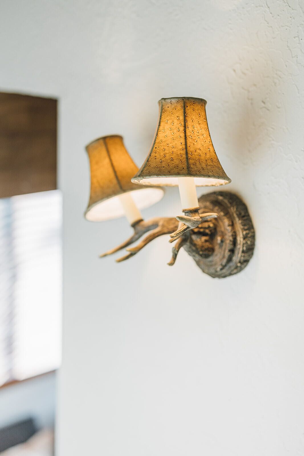 A wall-mounted lamp fixture with a rustic design, featuring a textured lampshade and a decorative base resembling a twisted branch.