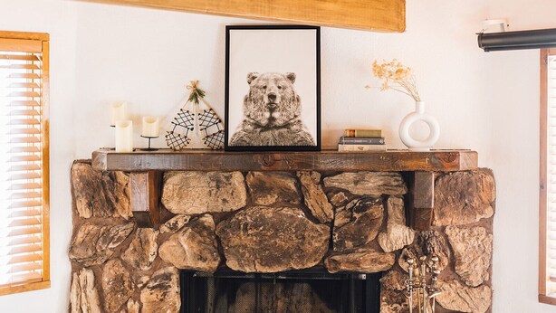 Una chimenea de piedra con un cuadro de un oso enmarcado, velas y adornos en la repisa.