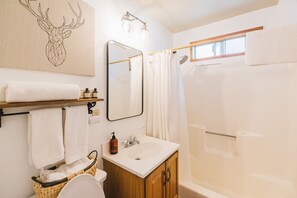 A bathroom with a wooden cabinet, a white sink, a mirror, a shower curtain, and a towel rack.