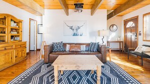 Una sala de estar acogedora con un sofá de cuero marrón, una mesa de centro de madera, alfombra estampada y un aparador con estantes.