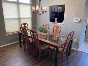 A dining area with a glass-top table surrounded by wooden chairs, a chandelier, and a potted plant.
