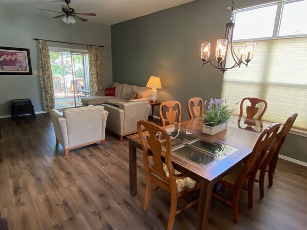 A dining area with a glass-top table, wooden chairs, and a chandelier.