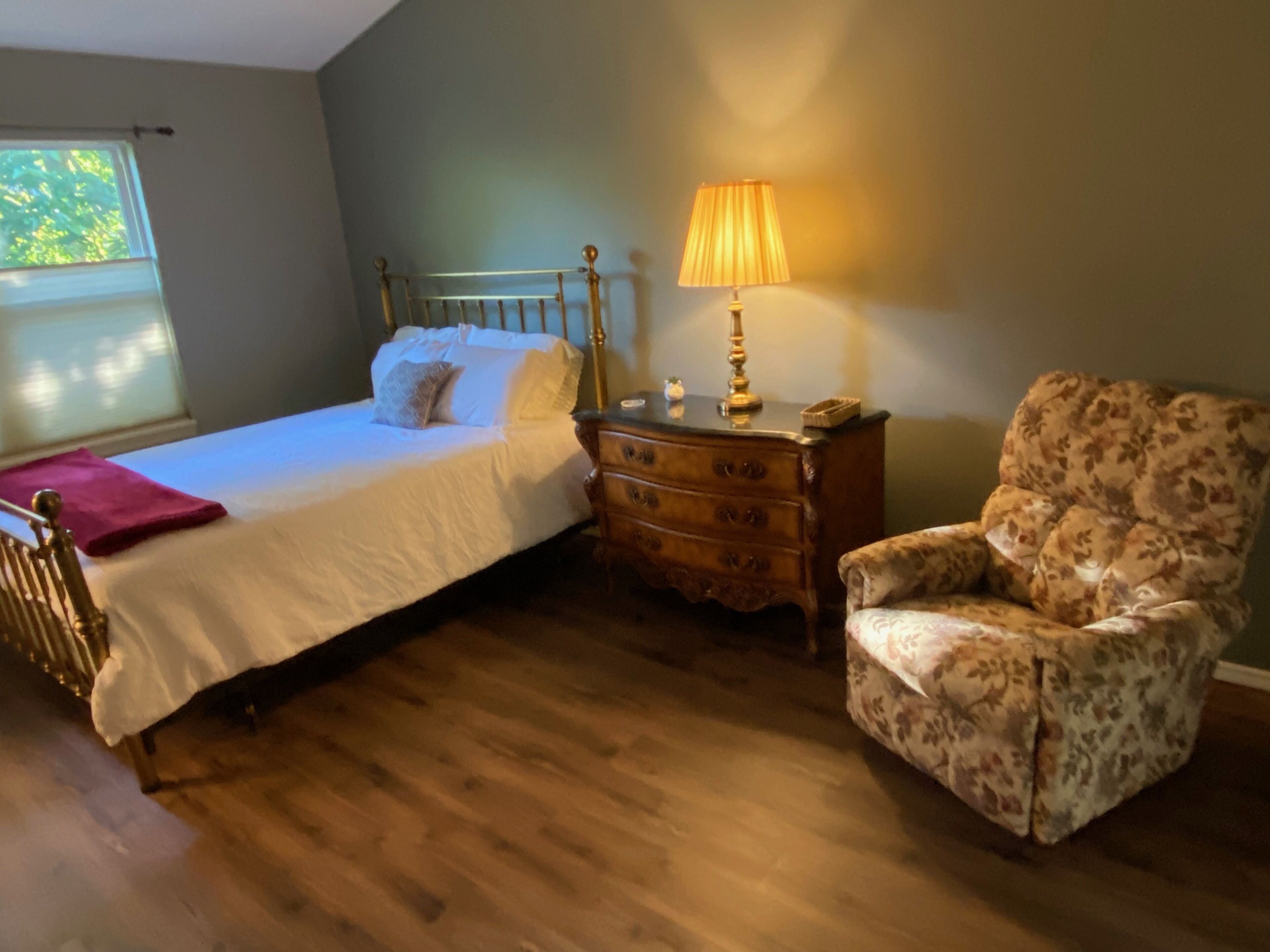 Quarto com uma cama, cômoda de madeira, uma cadeira e abajur.