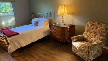 Quarto com uma cama, cômoda de madeira, uma cadeira e abajur.