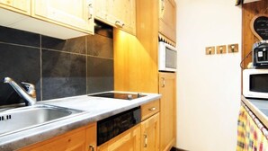 Une cuisine de taille réduite, dotée de meubles en bois, d’un évier à deux bacs et d’un four à micro-ondes.