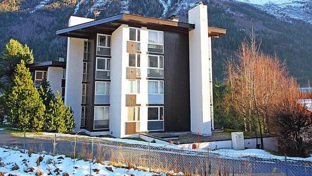 Un bâtiment moderne à plusieurs étages, doté de grandes fenêtres et d’un toit plat, entouré de montagnes et d’arbres couverts de neige.