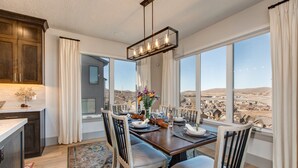 Comedor con vistas a un paisaje desértico, sillas de madera, candelabro y un ventanal grande.