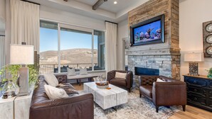 Una sala de estar con chimenea de piedra, muebles de cuero, un televisor grande y vistas al exterior.