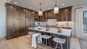 Una cocina moderna con alacenas de madera oscura, una isla grande con taburetes, iluminación colgante y vistas al exterior.