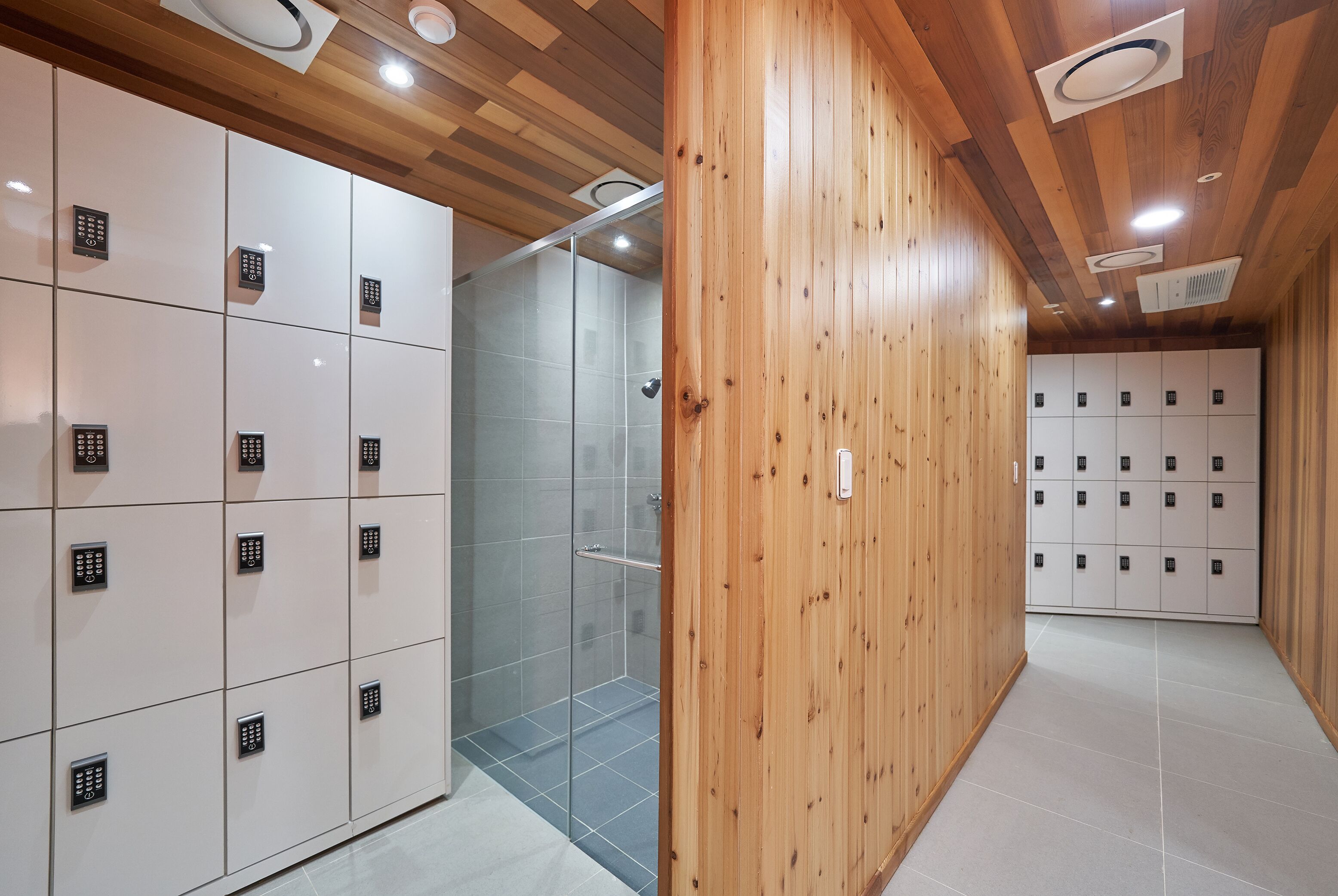 A modern locker room with wooden paneling and a glass shower enclosure.