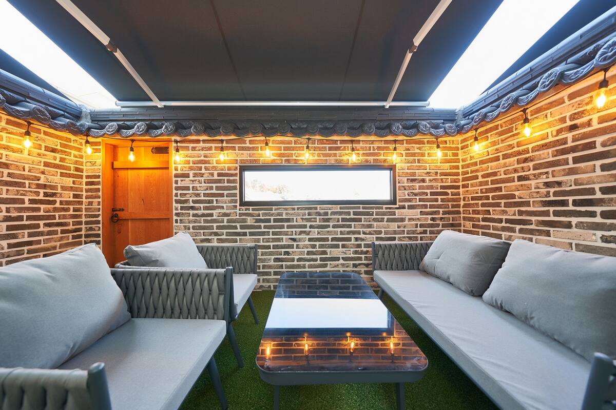An outdoor seating area with brick walls, a wooden door, and string lights.