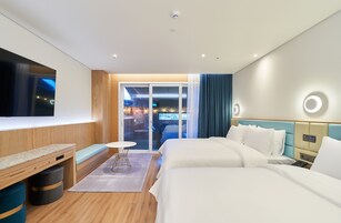 Une chambre d’hôtel moderne, dotée d’un grand lit, d’un bureau, d’une télévision et offrant une vue sur l’extérieur.